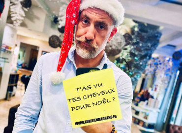 Aurélien Magnano, coiffeur-barbier à Montauban, portant un bonnet de Noël et tenant un message humoristique “T’as vu tes cheveux pour Noël ?” dans son salon décoré pour les fêtes.